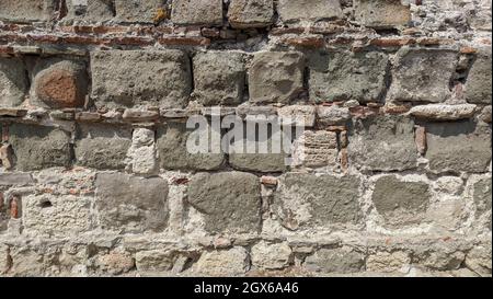 Steinmauer. Kleine Ziegel sind zwischen großen Steinen platziert. Fragment einer alten Burg Stockfoto