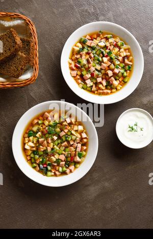 Kalter Sommer Okroshka Suppe mit Wurst, Gemüse und Kvass auf braunem Steingrund. Draufsicht, flach liegend Stockfoto