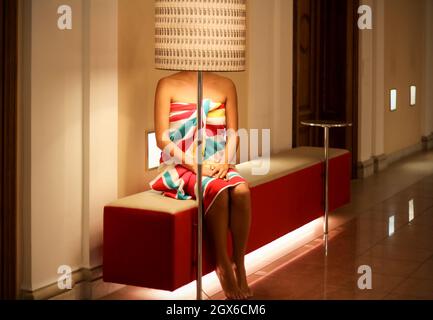 Konzept: Beleuchtung. Ziemlich kühne junge Frau in einem hellen Handtuch, sitzt auf der Bank Stockfoto