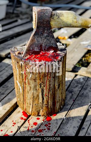 Eine Axt und ein alter Stumpf mit Spuren von Blut und Federn. Schlachtung von Geflügel. Eine Axt steckte in einem Stumpf fest. Stockfoto