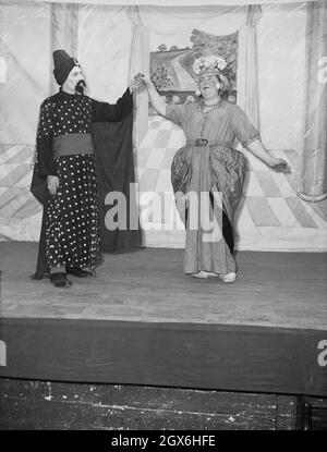 1957, historisch, zwei männliche Schauspieler auf der Bühne im Stück Aladdin, basierend auf einer nahöstlichen Volksgeschichte oder Fabel über den Sohn einer armen Witwe in china, der Besitzer einer magischen Lampe wird, England, Großbritannien. Ein Schauspieler spielt den Genie, während der andere Widow Twankey ist, eine weibliche Figur, die von einem Mann gespielt wird. Die Geschichte von Aladdin wurde 1788 erstmals in Covent Garden, London, aufgeführt. Stockfoto