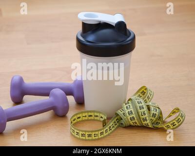 Ein Protein-Shaker mit einem Maßband und Gewichten in der Nähe. Nahaufnahme. Stockfoto