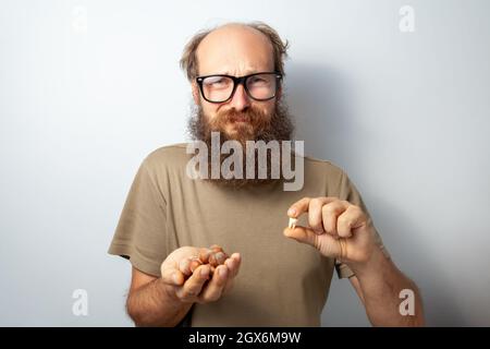 Mann, der nach dem Haselnussriß einen Zahn verloren hat, blickt mit runzelndem Gesicht auf die Kamera, leidet unter Schmerzen, kahlbärtiger Mann mit T-Shirt und Brille. Innenaufnahme des Studios isoliert auf grauem Hintergrund. Stockfoto