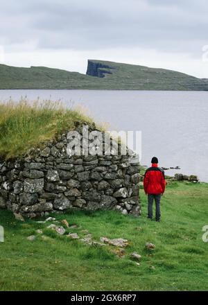 Ein einsamer Mann steht in der Nähe von mit Rasen bedeckten Häusern in der Nähe von Sorvagsvatn oder Leitisvatn See auf den Färöer Inseln Stockfoto