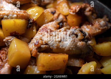 Gebratene Hähnchenflügel mit Kartoffeln werden in einer Pfanne in Nahaufnahme mit geringer Schärfentiefe gekocht Stockfoto