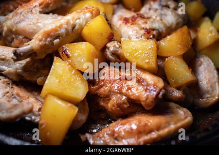 Gebratene Hähnchenflügel mit Kartoffeln werden in einer Pfanne in Nahaufnahme mit geringer Schärfentiefe gekocht Stockfoto