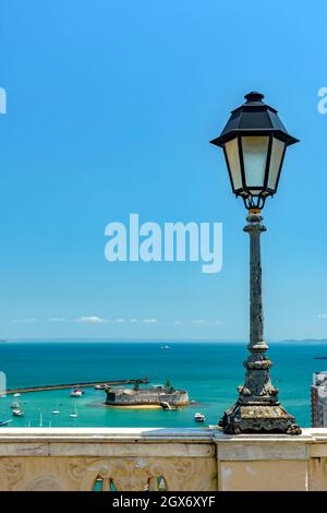 Alter Laternenpfosten an einer Wand mit Blick auf das Meer und die historische Festung in Todos os Santos Bay in Salvador, Bahia Todos os Santos Bay in Salvador, Bahia Stockfoto