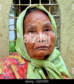 Eine traurig aussehende ältere Frau aus Minangkabau, die ein grünes Hijab- und Blumenkleid an einer gelben Wand in Bukittinggi, West Sumatra, Indonesien trägt. Stockfoto