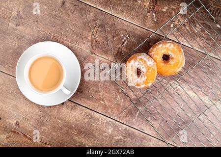 Holztischplatte mit einer Tasse Tee und frisch gebackenen Donuts auf einem Drahtkühlgestell Stockfoto