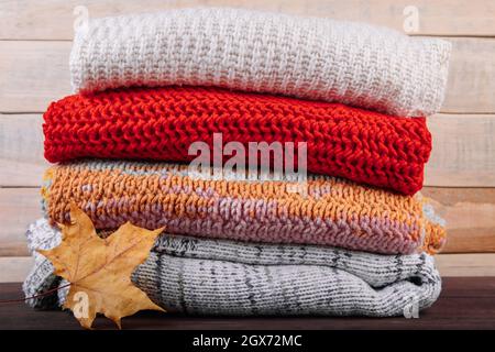 Stapel warmer Strickpullover. Herbstkonzept. Wollspringer und Ahornblatt auf einem hölzernen Hintergrund. Stockfoto