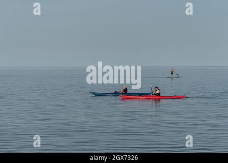 Zwei alte Männer paddeln mit dem Kajak auf dem ruhigen Meer und ein Mann auf einem Paddelbrett im Hintergrund, Vejle, Dänemark, 31. August 2021 Stockfoto