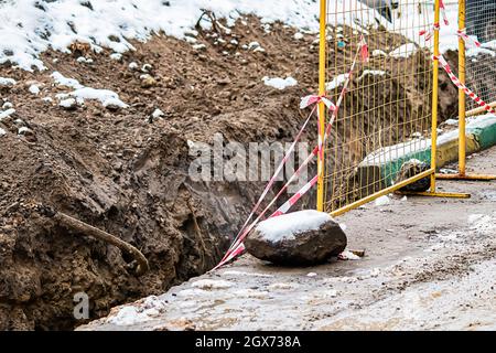 Reparatur von unterirdischen Versorgungseinrichtungen im Winter. Graben im Boden, eingezäunt mit einem Gitter. Verlassene Baustelle. Stockfoto