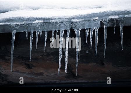 Eiszapfen auf dem Dach. Gefährliche Vereisung. Eisstalaktiten auf dem Haus. Schlechte Instandhaltung von Wohngebäuden im Winter. Stockfoto