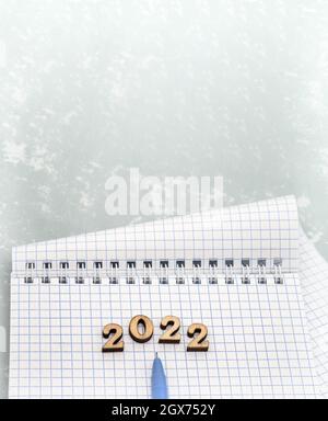 Notizbuch und Stift auf der grauen. Holznummern datieren 2022. Ein leeres Blatt Papier und ein blauer Stift. Stockfoto