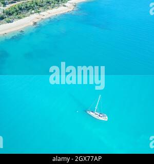 Farbenfrohe blaue Collage einer Yacht, die auf dem Meer und einem tropischen Sandstrand verankert ist Stockfoto