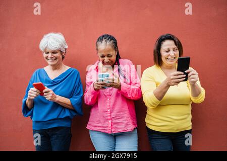 Ältere Menschen, die Spaß mit Mobiltelefonen im Freien haben - ältere Menschen, Konzept der Technologieabhängigkeit - Fokus auf afrikanisches Frauengesicht Stockfoto