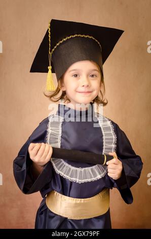 Schönes kleines Mädchen glücklich mit ihrem Abschluss. Gekleidet mit ihrer Abschlussmütze und Diplom in der Hand. Stockfoto