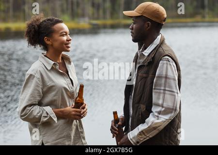 Seitenansicht des Porträts eines jungen afroamerikanischen Paares, das im Freien plaudert, während es am See steht Stockfoto
