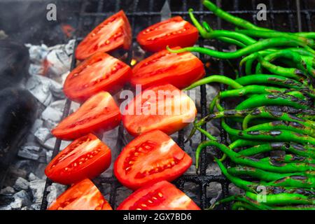 Dünne grüne Paprika und Tomaten auf Holzkohlegrill. Schwarze Grillflecken bestehen aus Grill. Veganer Grill Stockfoto