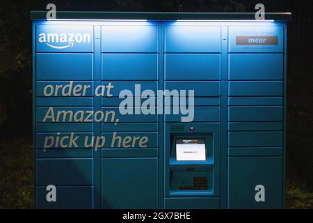 Amazon Hub locker gesehen in der Nacht auf dem Parkplatz des Kenley Bahnhof, South London. Stockfoto