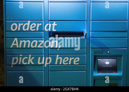 Amazon Hub locker gesehen in der Nacht auf dem Parkplatz des Kenley Bahnhof, South London. Stockfoto