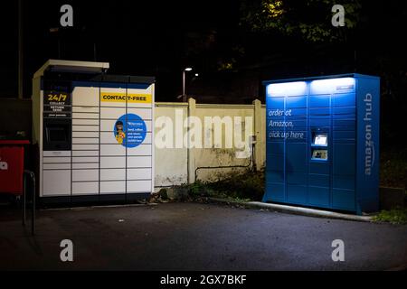 InPost Paketabholung Schließfach und ein Amazon Hub locker gesehen in der Nacht auf dem Parkplatz des Kenley Bahnhof, South London. Stockfoto