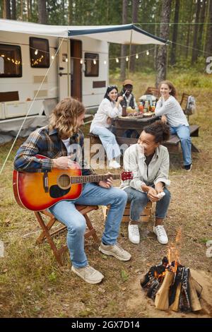 Vertikales Porträt eines jungen Paares, das beim Campen mit Freunden im Wald Gitarre spielt Stockfoto