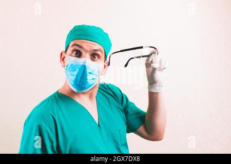 Doktor in grünem Chirurgen Anzug und schützende Atemmaske mit Schutzbrille in der Hand isoliert Stockfoto