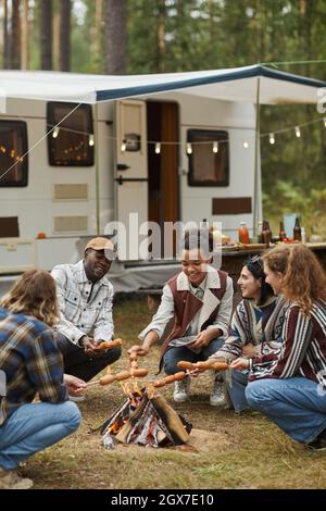 Vertikale Ganzkörperportrait von jungen Menschen, die Marschwalben rösten, während sie mit Freunden im Wald campen Stockfoto