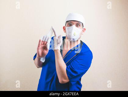 Arzt mit weißen Gluten an den Händen in blauem Chirurgen-Anzug und schützender Atemmaske isoliert Stockfoto
