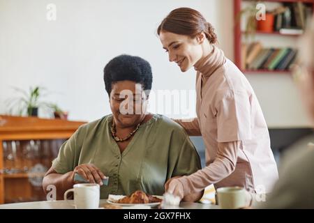 Porträt einer lächelnden jungen Frau, die sich im Pflegeheim um eine ältere afroamerikanische Dame kümmert, Kopierraum Stockfoto