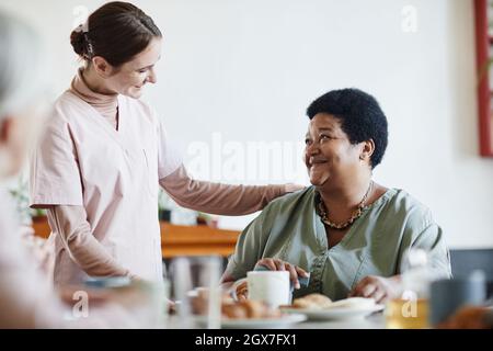 Porträt einer lächelnden jungen Frau, die sich im Pflegeheim um ältere afroamerikanische Patienten kümmert, Kopierraum Stockfoto