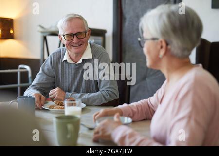 Porträt eines weißhaarigen älteren Mannes, der fröhlich lächelt, während er das Frühstück im Speisesaal des Pflegeheims genießt, Platz zum Kopieren Stockfoto