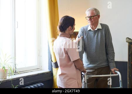 Porträt einer fürsorglichen jungen Frau, die einem älteren Mann mit Gehhilfe im Pflegeheim hilft, Kopierraum Stockfoto