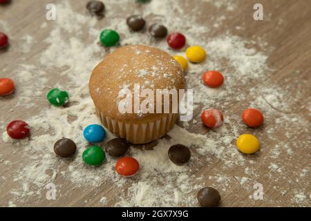 Gebackene Muffins mit verschiedenfarbigen Pralinen, bestäubt mit Zucker, köstliche Desserts mit Details in der Textur Stockfoto