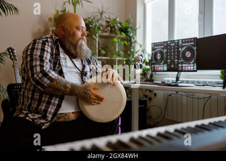 Talentierter Mann spielt Trommel sitzen am Arbeitsplatz mit Computermonitoren im Studio Stockfoto