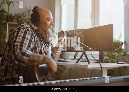 Reifer Komponist spielt am Arbeitsplatz im Heimstudio Basgitarre-Aufnahmen Stockfoto