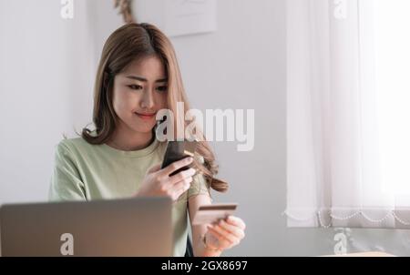 Zugeschnittenes Bild einer lächelnden Millenniumsfrau mit Smartphone und Bankkreditkarte, die zu Hause beim Online-Shopping mit Mobilgeräten mitgewirkt hat, einer glücklichen Shopper-Frau Stockfoto