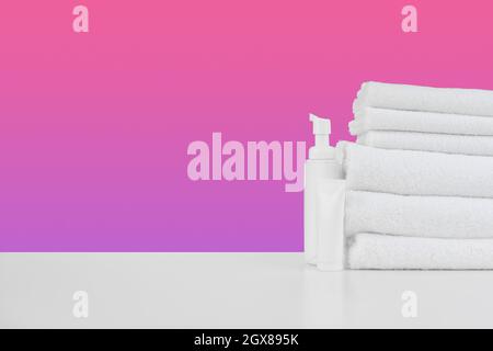 Stapel Handtücher, Flaschen mit Shampoo auf weißem Tisch Stockfoto