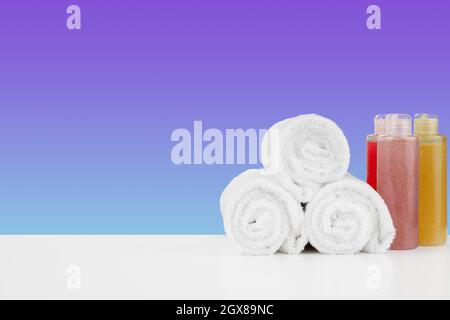 Stapel Handtücher, Flaschen mit Shampoo auf weißem Tisch Stockfoto