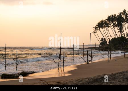 Panoramablick auf traditionelle Fischer Stelzenstöcke zum Angeln im Meer wavesat Sonnenuntergang in der Nähe von Mirissa, Ahangama, Sri Lanka. Stockfoto