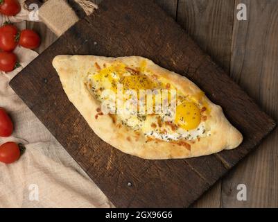 Gebackene Adjarian-Khachapuri mit VollEigelb auf Holzbrett, traditionelles Gericht, Draufsicht Stockfoto