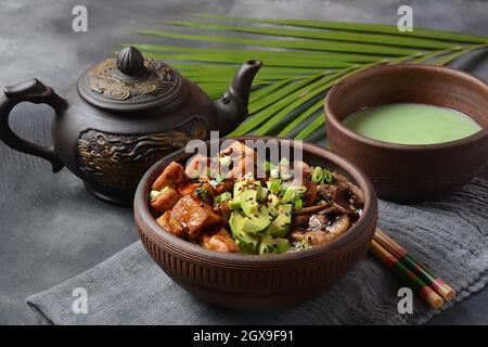 Süßer, würziger, knuspriger und gebratener Tofu in einer Schüssel mit Terriayaki-Sauce, Avocado, gebratenen Pilzen, Sesamsamen und Reis. Serviert mit grünem Matcha-Tee. Stockfoto