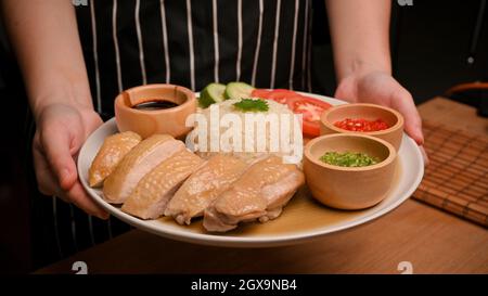 Bild einer asiatischen Küche. Eine weibliche Kellnerin serviert Hainanesischen Hühnerreis mit Chilisauce und süßer Sojabohnensauce. Stockfoto