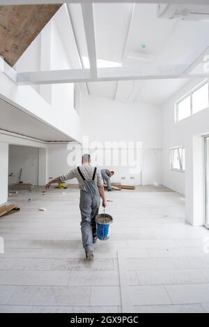 Fachkräfte, die die keramischen Holz-Effekt-Fliesen auf dem Boden Installieren, Arbeiter, die Laminatboden auf der Baustelle der neuen Wohnung machen Stockfoto