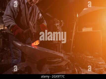 Traditionelle Schmied manuell Schmieden die Red Hot geschmolzenes Metall auf dem Amboss mit Sonnenlicht durch die Fenster in der Schmiede Werkstatt. Schmied arbeiten Stockfoto