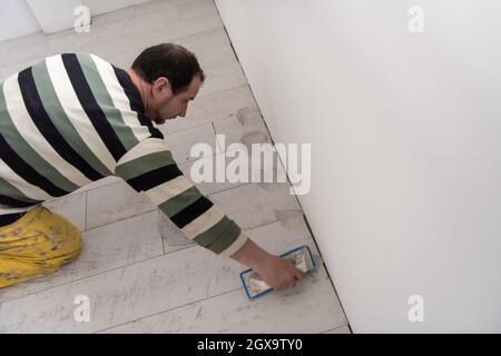 Verfugen von Keramikfliesen. Tiler füllen den Raum zwischen Keramikfliesen aus Holz mit einem Gummi-Trowel auf dem Boden in einer neuen modernen Wohnung Stockfoto