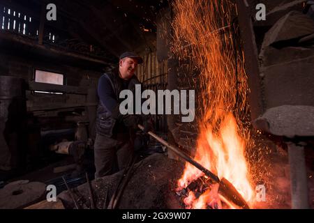 Jungen traditionellen Schmied Arbeiten mit offenen Flammen Feuer der Schmiede in der Schmiede mit Funken Feuerwerk schmieden heißes Eisen in der Werkstatt Stockfoto