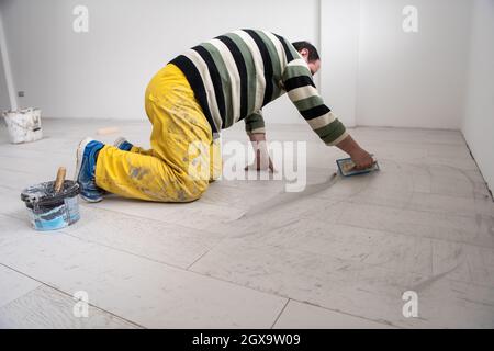 Verfugen von Keramikfliesen. Tiler füllen den Raum zwischen Keramikfliesen aus Holz mit einem Gummi-Trowel auf dem Boden in einer neuen modernen Wohnung Stockfoto