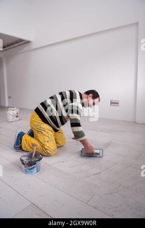 Verfugen von Keramikfliesen. Tiler füllen den Raum zwischen Keramikfliesen aus Holz mit einem Gummi-Trowel auf dem Boden in einer neuen modernen Wohnung Stockfoto